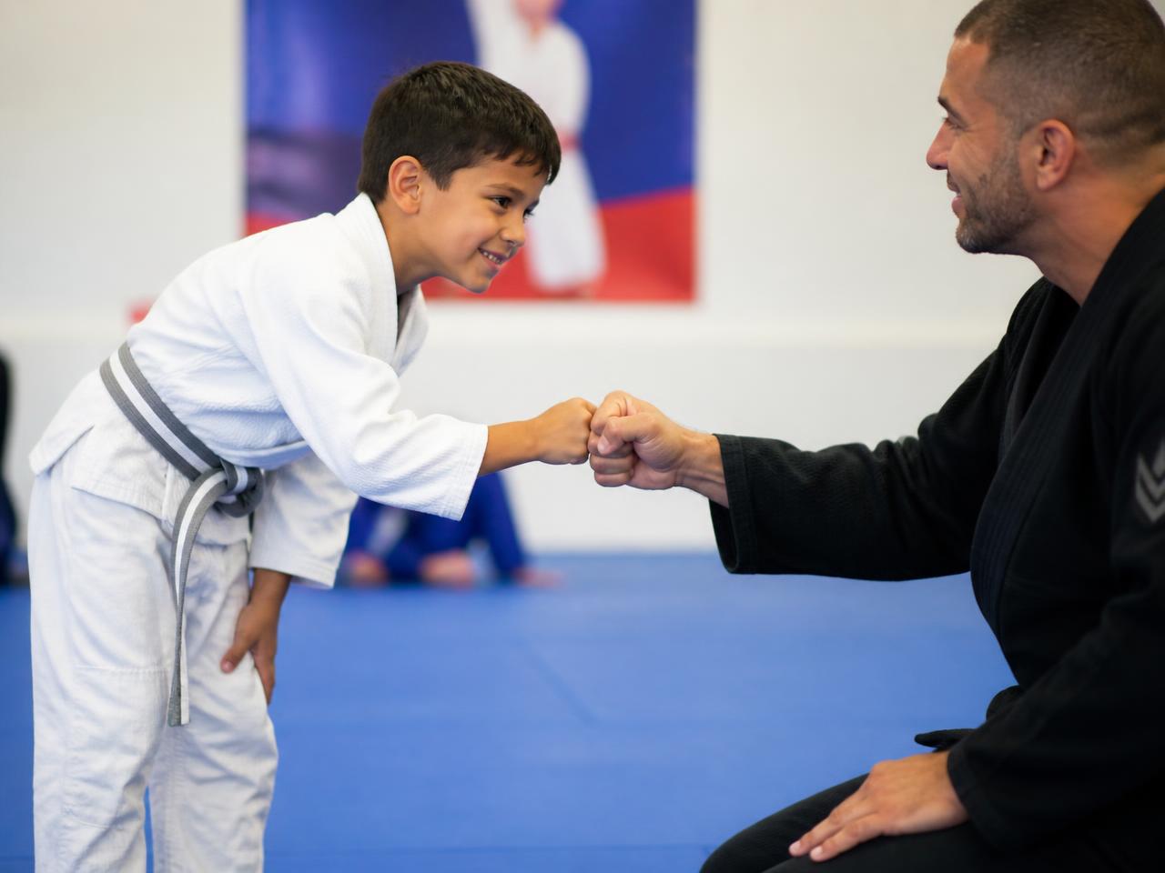 Young Little Champion bowing in and fist-bumping his coach on the mat