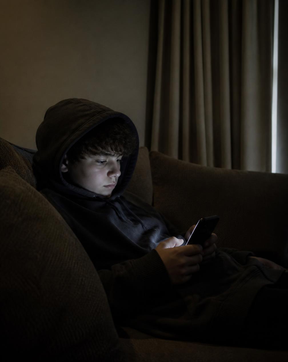 A teenager withdrawn on the couch with a phone